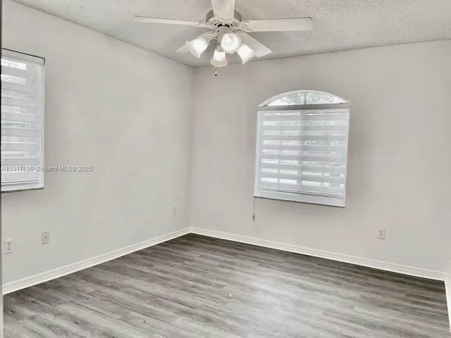 an empty room with wooden floor chandelier fan and windows