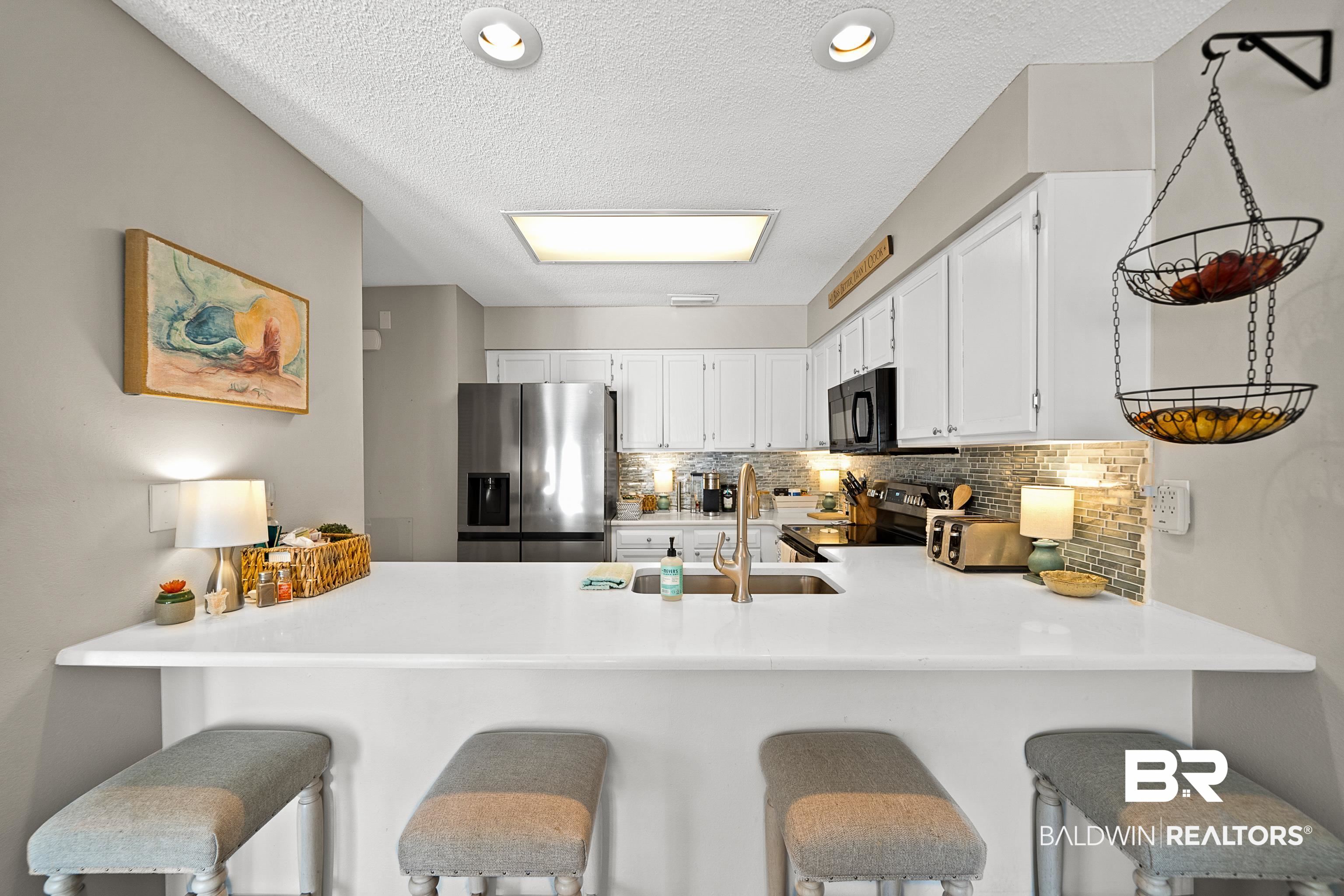 1701 Regency Road, Unit 106 Gulf Shores, AL 36542 - Photo 16 of 42 Kitchen featuring a textured ceiling, appliances with stainless steel finishes, tasteful backsplash, white cabinetry, and a kitchen breakfast bar