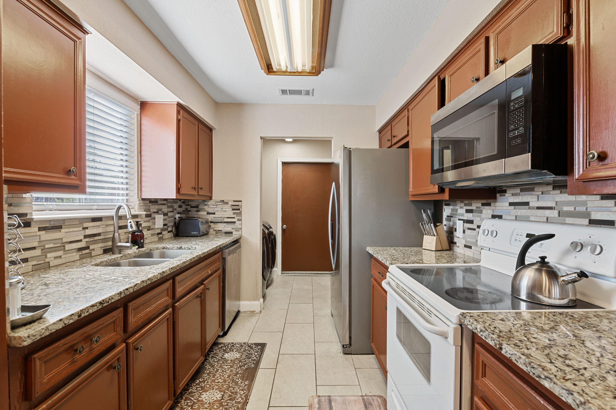 1602 Plateau Ridge Cedar Park, TX 78613 - Photo 4 of 29 Kitchen featuring stainless steel appliances, light stone counters, light tile patterned floors, wood finish cabinetry, and washer and dryer