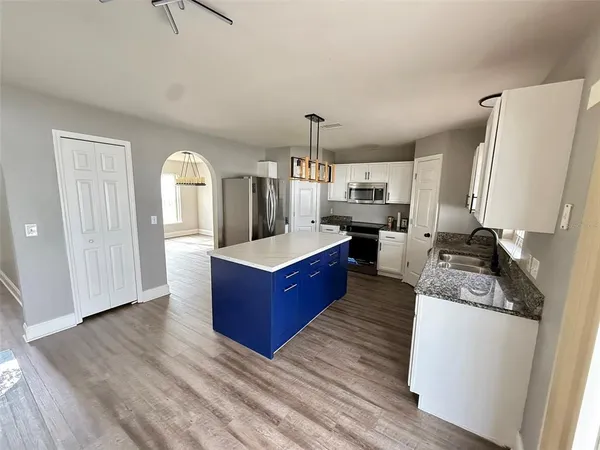 a large kitchen with stainless steel appliances kitchen island granite countertop a refrigerator a stove a sink dishwasher and white cabinets with wooden floor