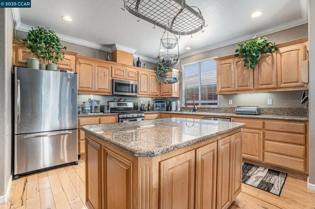 a kitchen with stainless steel appliances granite countertop a sink dishwasher a refrigerator and a dining table with wooden floor