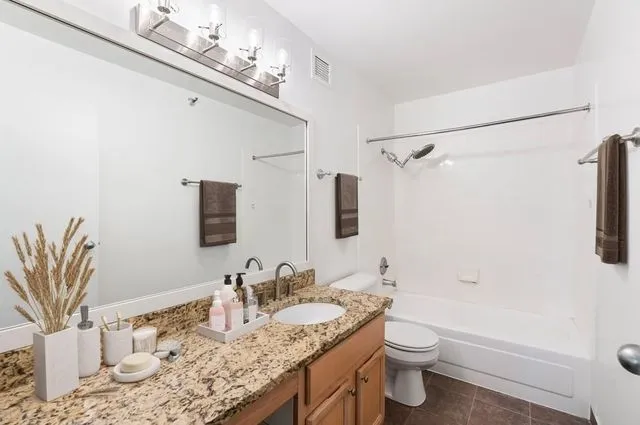a bathroom with a granite countertop sink a toilet a mirror and shower