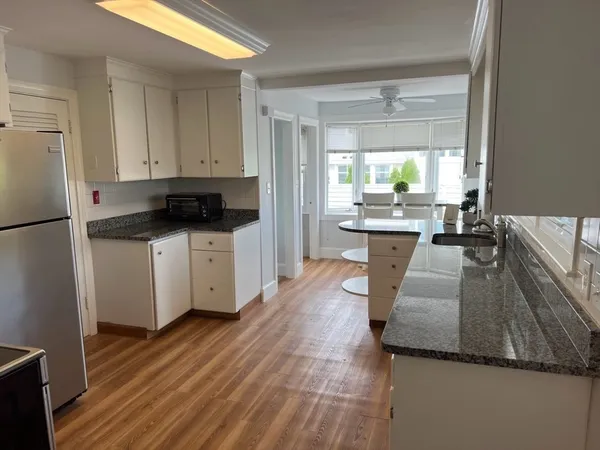 a kitchen with granite countertop a refrigerator a sink a stove and white cabinets with wooden floor