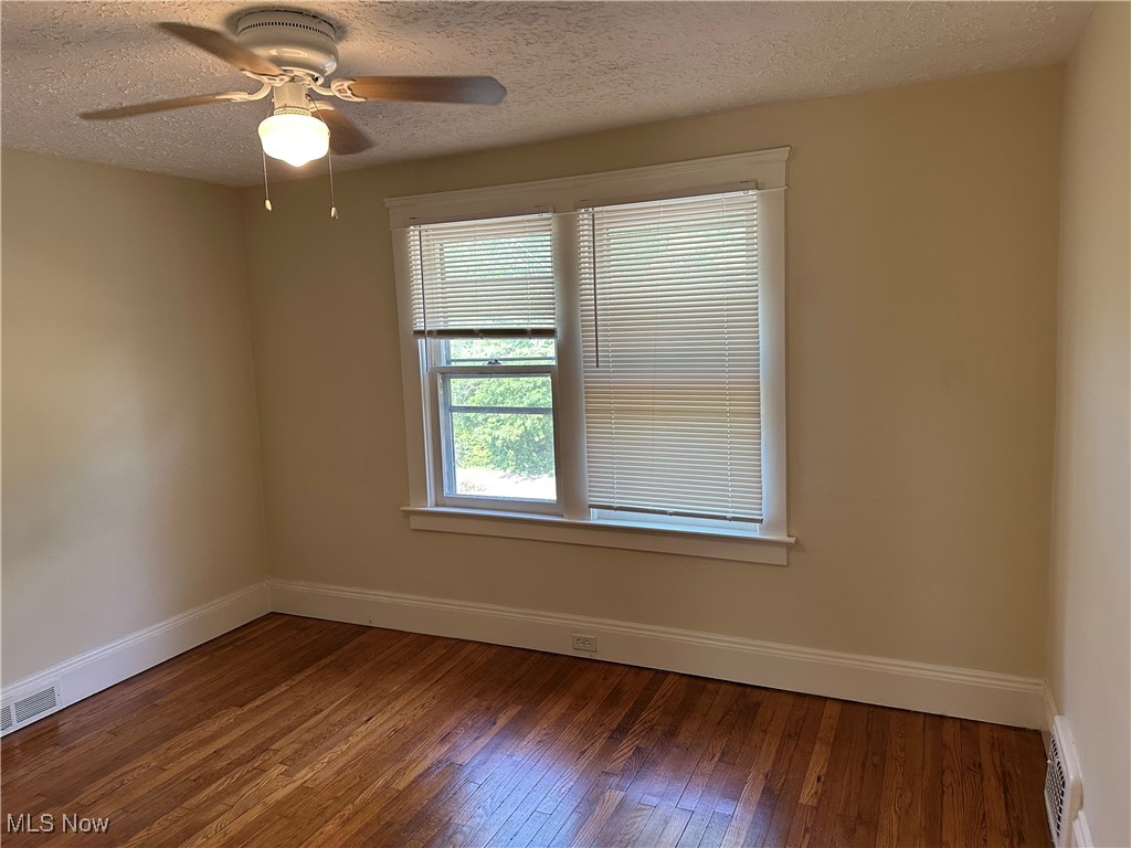 1596 Wood Road Cleveland Heights, OH 44121 - Photo 9 of 25 Empty room featuring healthy amount of natural light, hardwood / wood-style flooring, a ceiling fan, and a textured ceiling