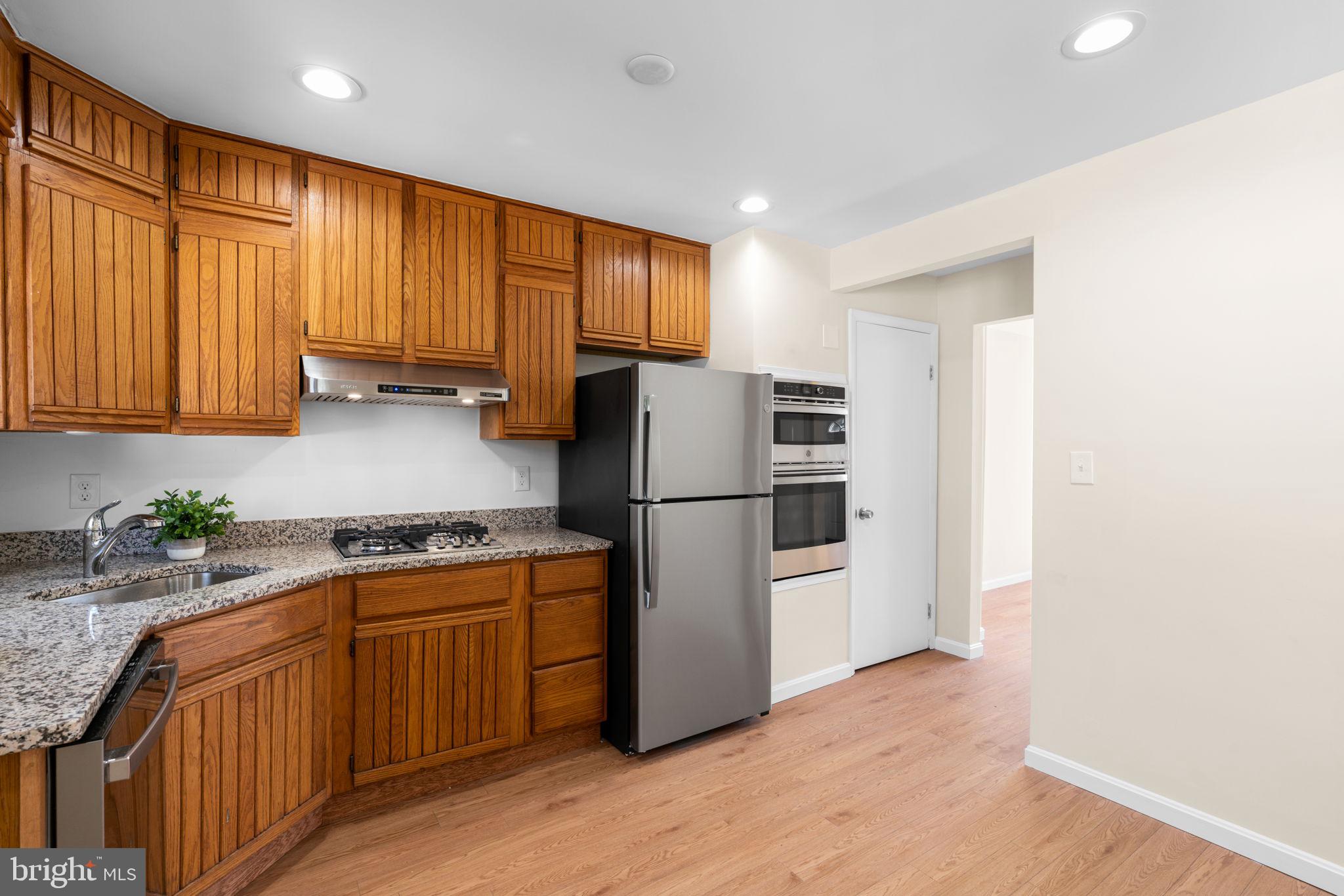 7134 Bexhill Road Windsor Mill, MD 21244 - Photo 12 of 34 a kitchen with stainless steel appliances granite countertop a refrigerator a sink dishwasher and wooden cabinets with wooden floor