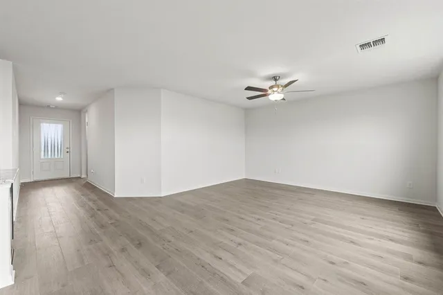 a view of an empty room with wooden floor and a ceiling fan
