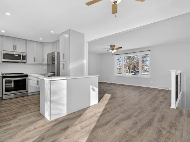 a kitchen with stainless steel appliances granite countertop a refrigerator a stove a sink dishwasher and white cabinets with wooden floor