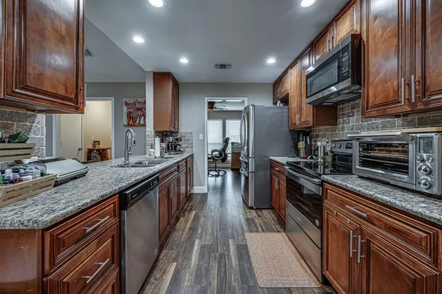 a large kitchen with stainless steel appliances granite countertop a stove top oven a sink dishwasher a dining table and chairs with wooden floor