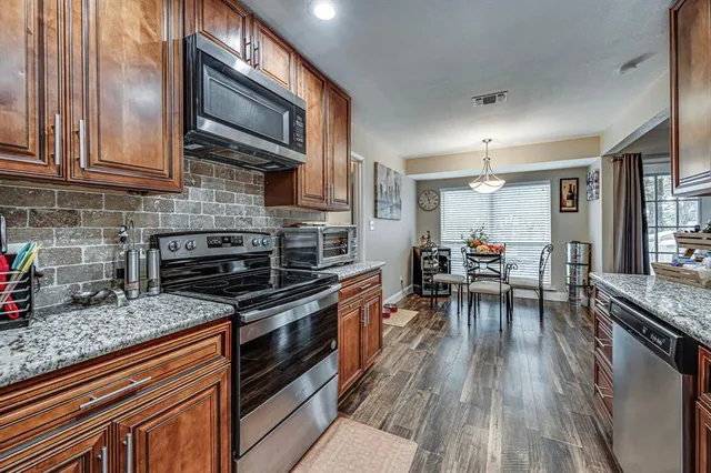 a kitchen with stainless steel appliances granite countertop a stove top oven a sink dishwasher a dining table and chairs with wooden floor