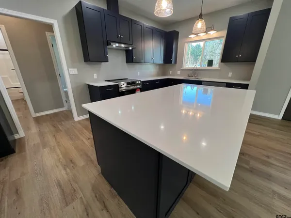 a large kitchen with stainless steel appliances a large counter top a wooden floor a stove and a refrigerator