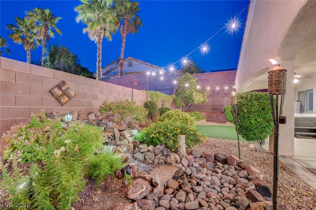 1604 Cattle Ranch Place Henderson, NV 89002 - Photo 92 of 99 A tranquil backyard oasis features string lighting, a soothing rock water feature, and low-maintenance landscaping.