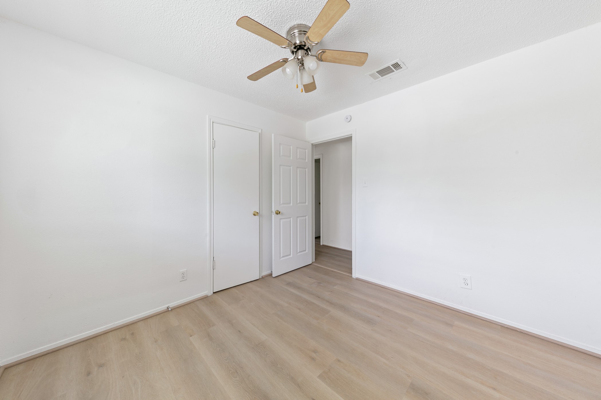 700 Lyle W Avenue, Unit D Cleveland, TX 77327 - Photo 7 of 16 This is a bright, minimal bedroom featuring light wood flooring, white walls, a ceiling fan, and a closet with a white door. Perfect for a clean, modern look.