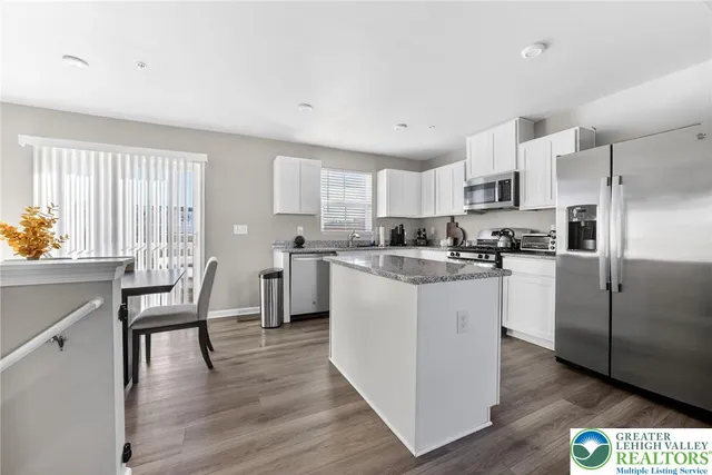 a kitchen with stainless steel appliances granite countertop a refrigerator a stove top oven a sink dishwasher and white cabinets with wooden floor