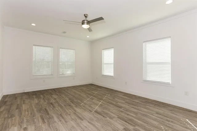 an empty room with wooden floor fan and windows
