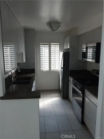 a kitchen with granite countertop stainless steel appliances a stove a sink a refrigerator white cabinets and wooden floor