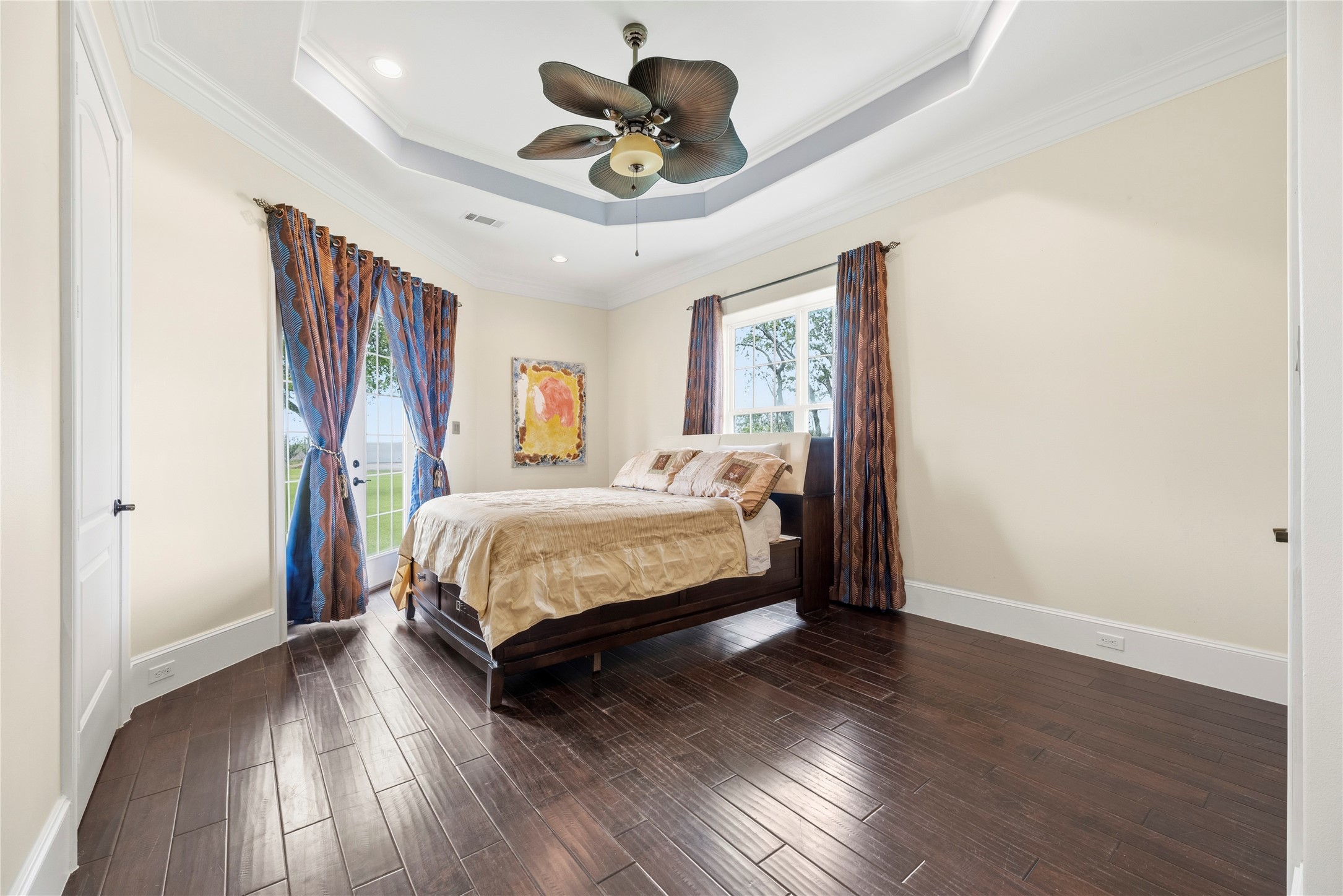 6306 Farm To Market 359 Fulshear, TX 77441 - Photo 22 of 44 This expansive bedroom features rich engineered wood flooring and a custom tray ceiling, offering private French door access to the verdant grounds for a refined guest experience