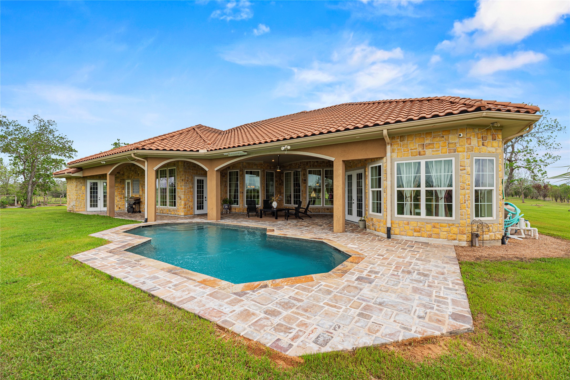 6306 Farm To Market 359 Fulshear, TX 77441 - Photo 29 of 44 This custom in-ground gunite pool is framed by an expansive stone patio and refined masonry, offering a sophisticated setting for outdoor relaxation with views of the lush, open acreage.