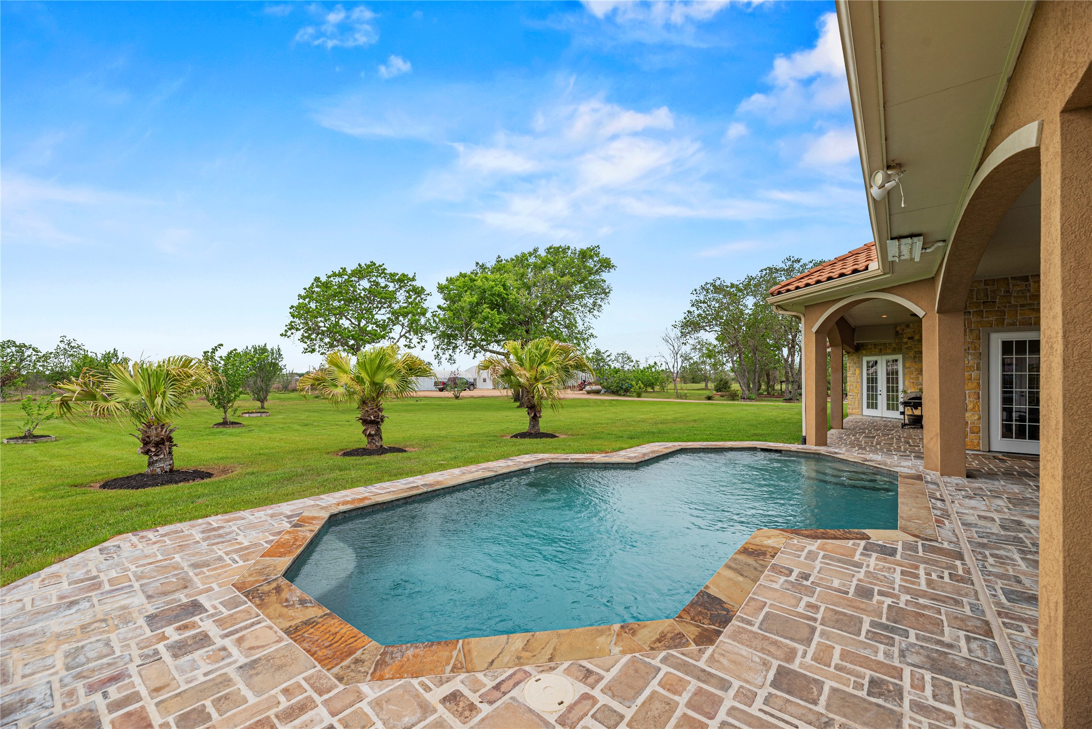 6306 Farm To Market 359 Fulshear, TX 77441 - Photo 3 of 44 The pristine 13,000-gallon freshwater gunite pool is bordered by an expansive stone terrace, providing an elite space for outdoor relaxation amidst the estate's private 12.6-acre grounds.