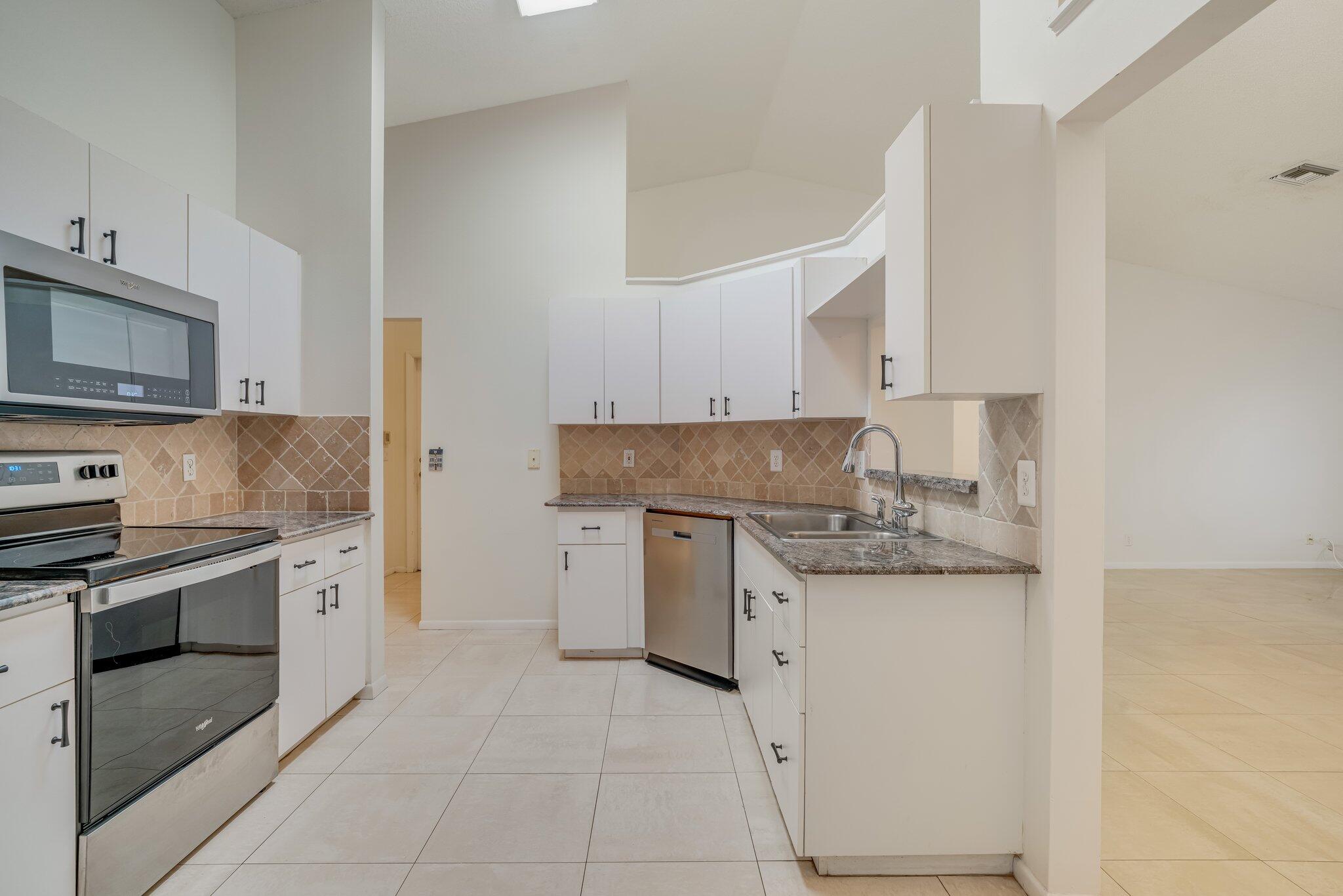 6209 Pond Tree Court Greenacres, FL 33463 - Photo 10 of 38 a kitchen with stainless steel appliances granite countertop a sink and dishwasher a stove top oven with white cabinets