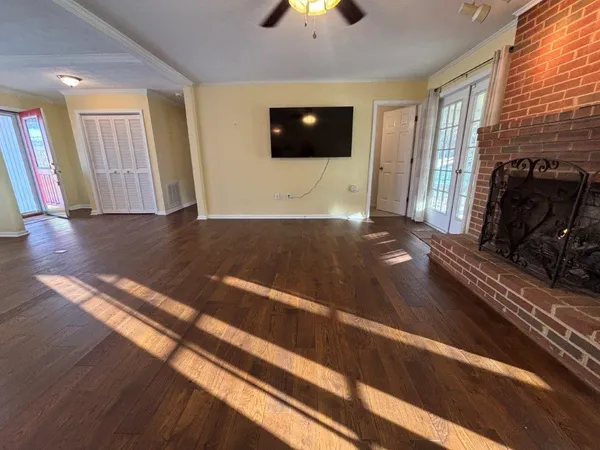 a view of a room with wooden floor fire place and windows