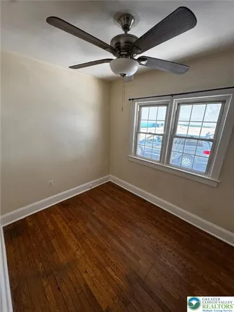 an empty room with wooden floor fan and windows