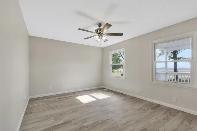an empty room with wooden floor chandelier fan and windows