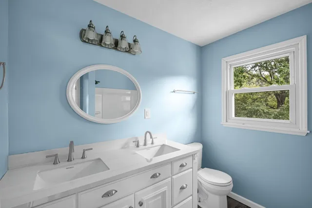 a bathroom with a toilet a sink a mirror and a window