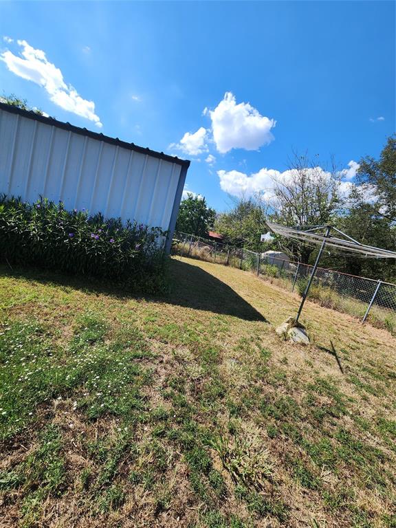 403 Barker Street Cumby, TX 75433 - Photo 12 of 16 Detached metal-sided structure with a sloped roof, surrounded by established shrubbery and a chain-link fence