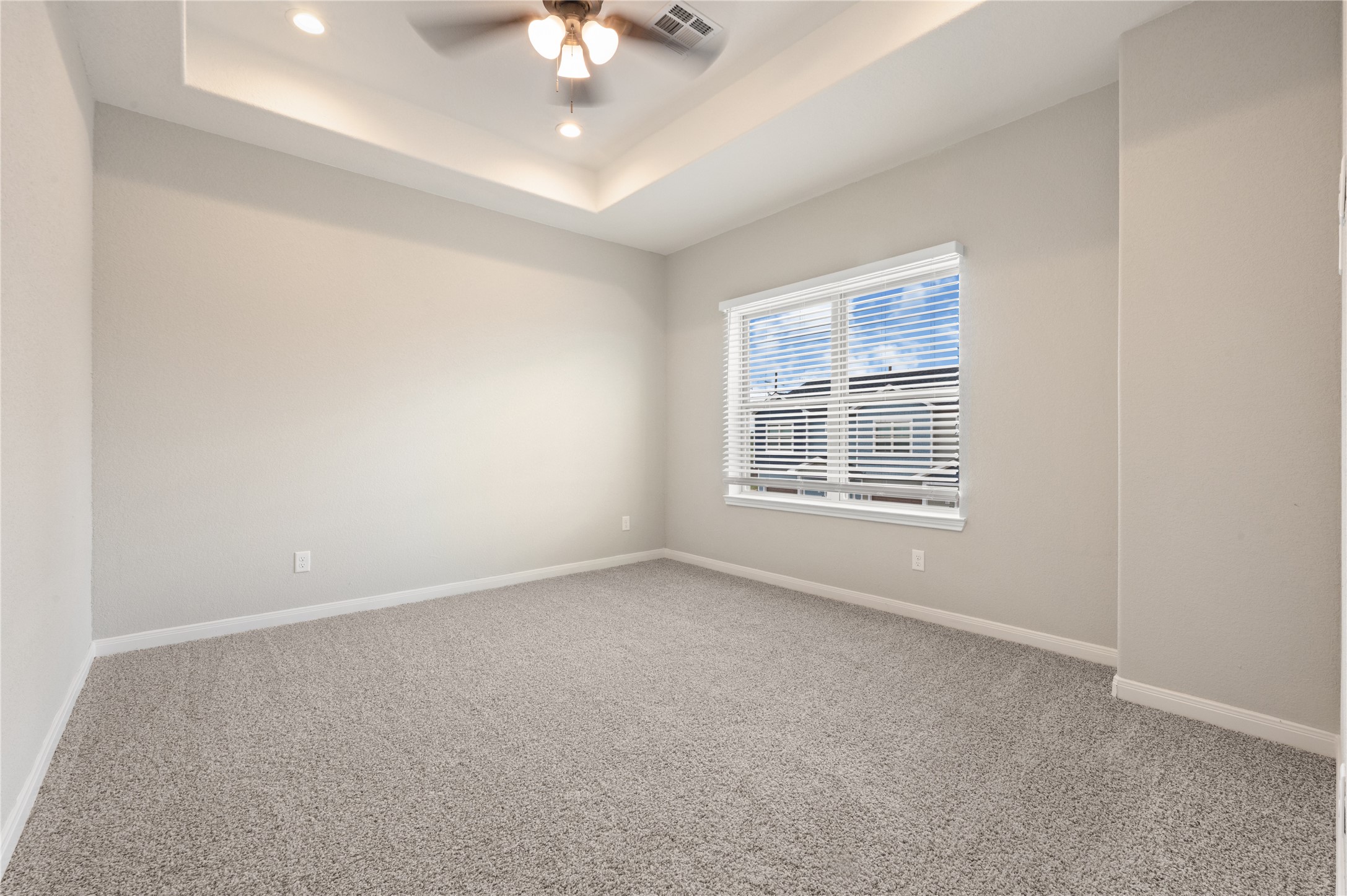 14010 Longstreet Road, Unit 2 Willis, TX 77318 - Photo 16 of 29 This photo showcases a bright, spacious bedroom with neutral walls, plush carpet, and a large window with blinds. The room features a tray ceiling with recessed lighting and a ceiling fan, creating a comfortable and airy atmosphere.