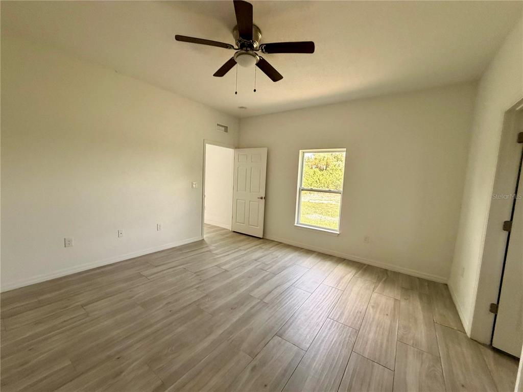 14142 Appleton Boulevard Port Charlotte, FL 33981 - Photo 9 of 26 an empty room with wooden floor ceiling fan and windows