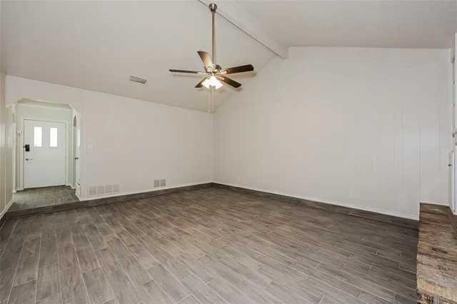an empty room with wooden floor fan and windows