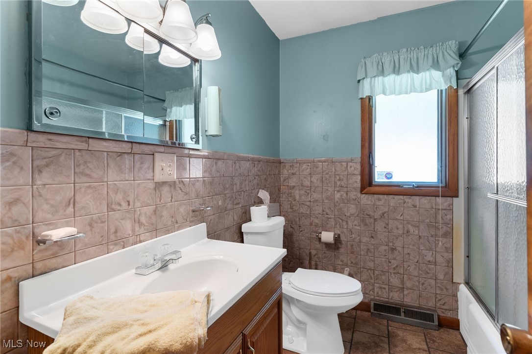 3907 Edwards Street Mineral Ridge, OH 44440 - Photo 23 of 45 Bathroom with bath / shower combo with glass door, tile walls, vanity, dark tile patterned flooring, and wainscoting