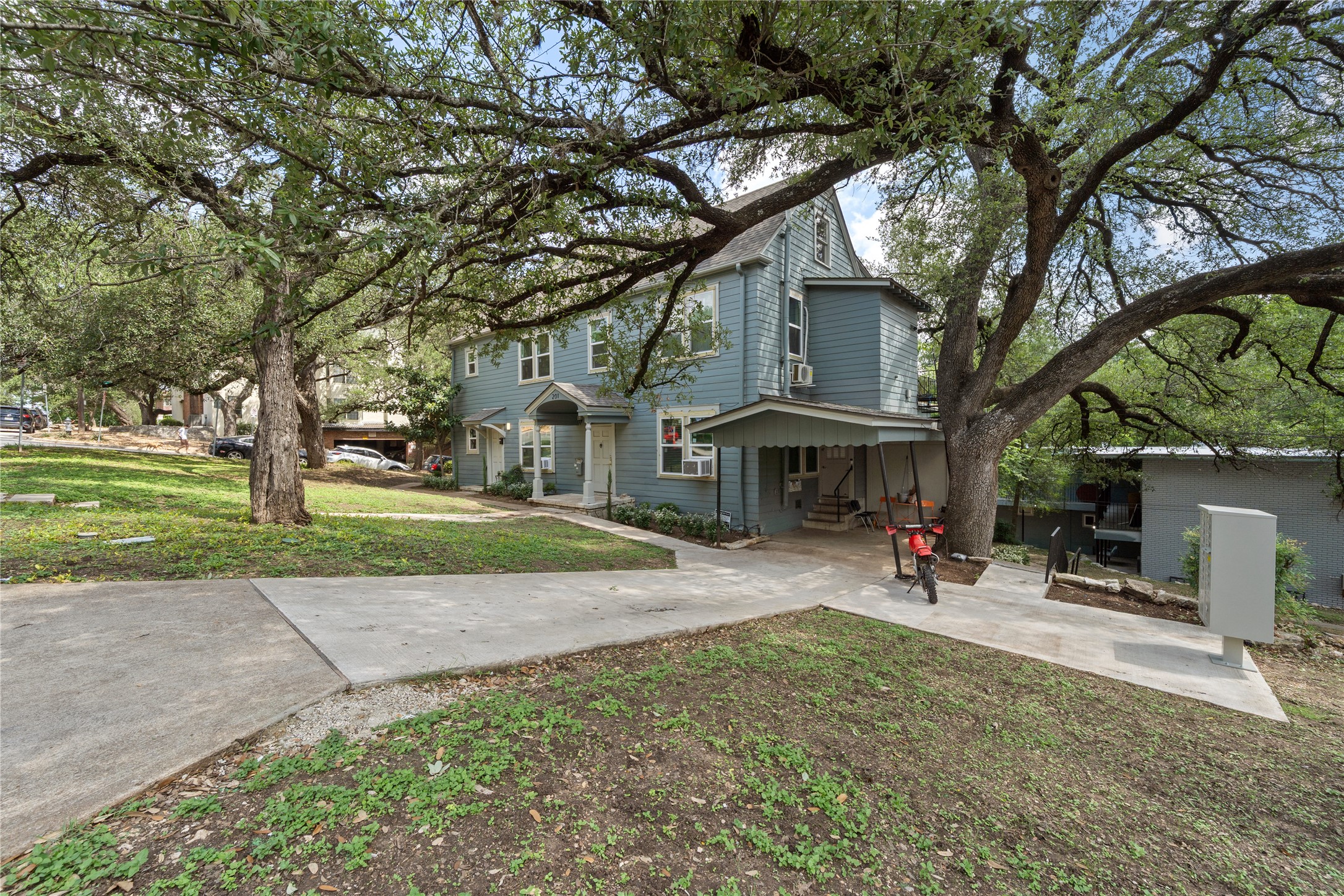 201 West 31st Street, Unit E Austin, TX 78705 - Photo 14 of 16 Mature trees shade this inviting light blue facade, offering a charming residential appeal.