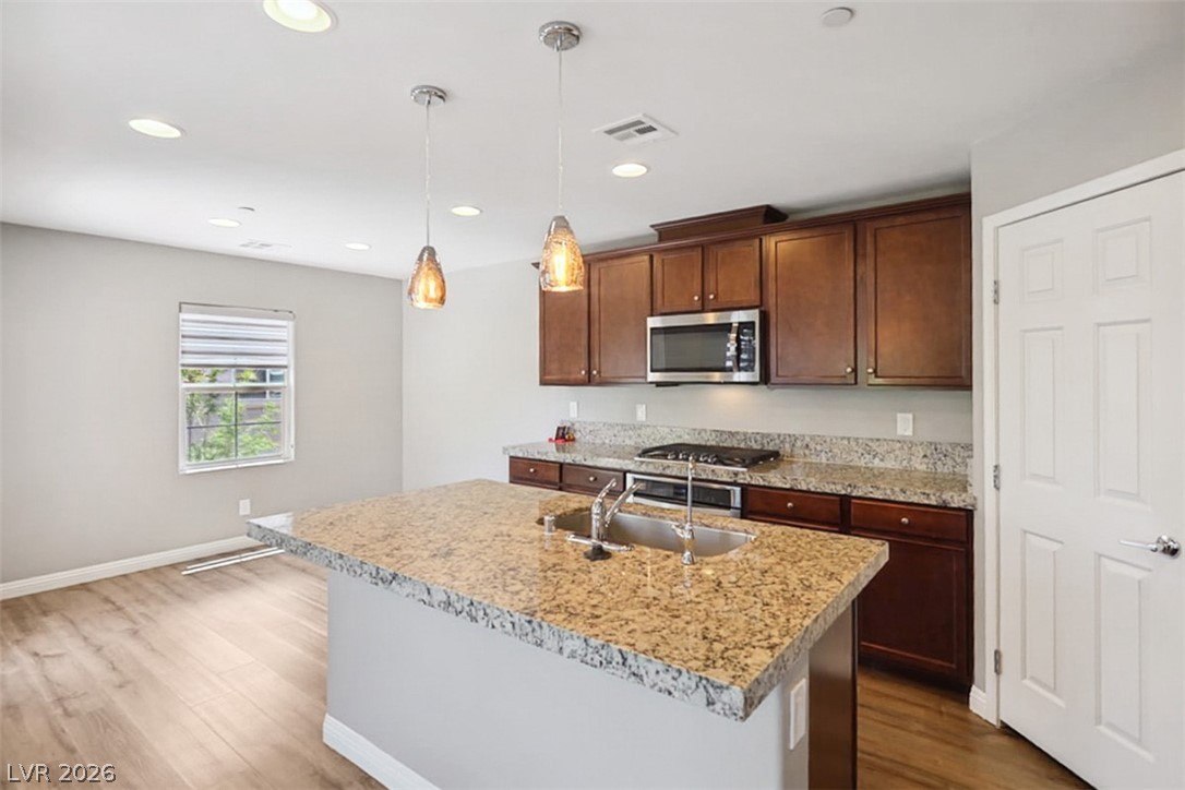 9940 Sable Point Street Las Vegas, NV 89178 - Photo 20 of 40 Kitchen featuring appliances with stainless steel finishes, a sink, wood finished floors, baseboards, and a kitchen island with sink