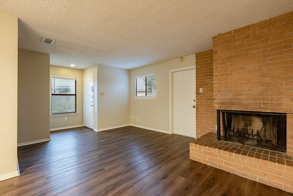 1205 Inland Greens, Unit B Austin, TX 78758 - Photo 3 of 16 Unfurnished living room with healthy amount of natural light, a fireplace, dark wood-style floors, and a textured ceiling