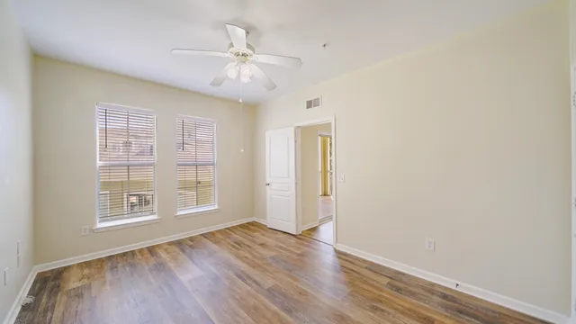 an empty room with wooden floor chandelier fan and windows