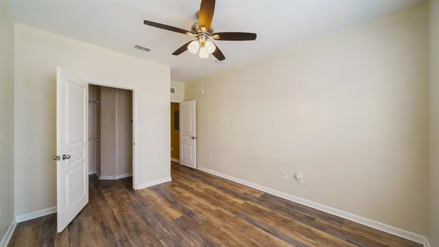 an empty room with wooden floor fan and windows