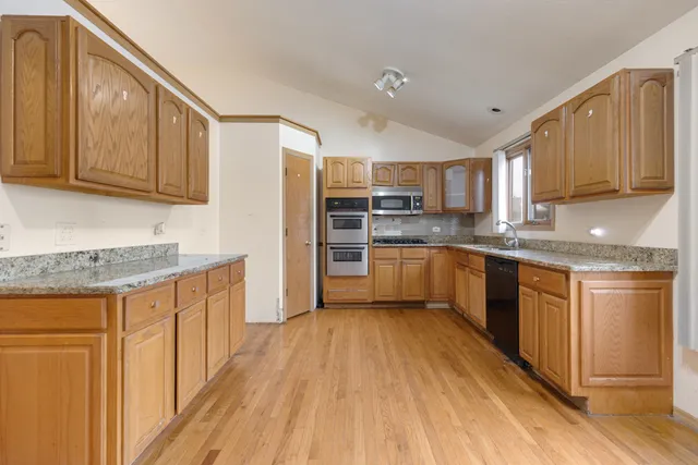 a kitchen with stainless steel appliances granite countertop wooden cabinets a sink a stove a refrigerator and island with wooden floor