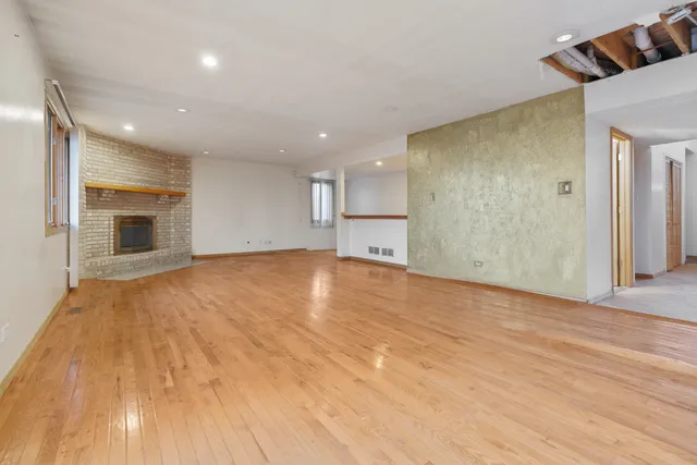 a view of empty room with wooden floor and kitchen