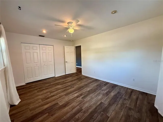 a view of an empty room with wooden floor and a ceiling fan