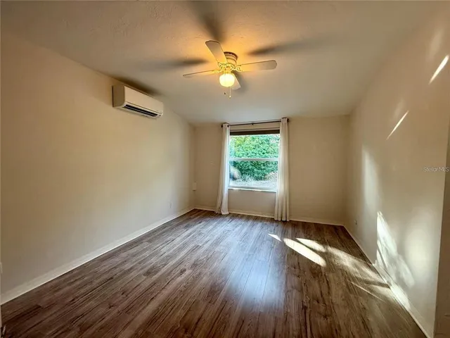 an empty room with wooden floor fan and windows