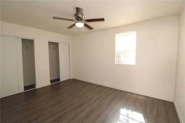 an empty room with wooden floor fan and windows