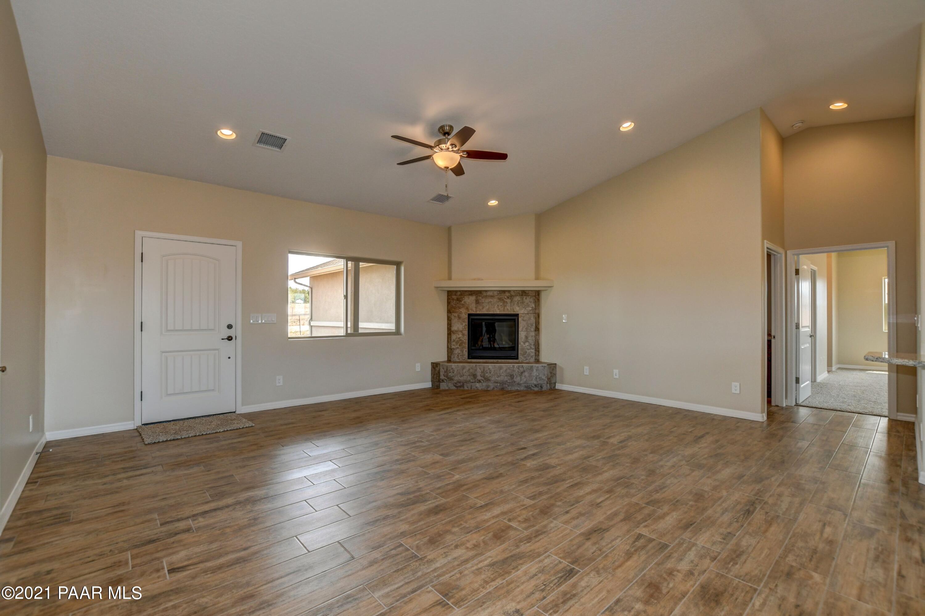 1495 Saddle Road Paulden, AZ 86334 - Photo 11 of 33 an empty room with wooden floor a ceiling fan a fireplace and windows