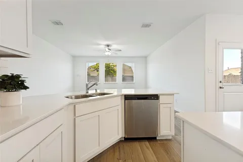 a kitchen with a sink dishwasher and white cabinets with wooden floor