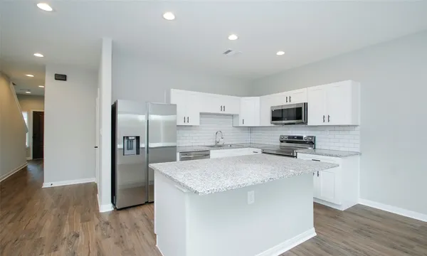 a kitchen with stainless steel appliances white cabinets a sink a stove a microwave and wooden floor