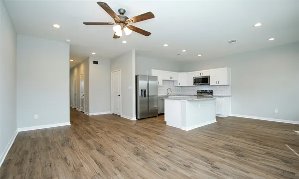 a view of kitchen with stainless steel appliances kitchen island wooden floors and white walls