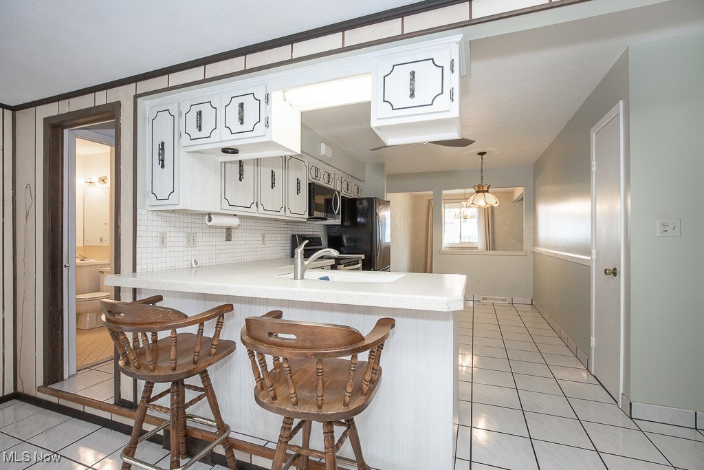 4569 McFarland Road Cleveland, OH 44121 - Photo 4 of 29 Kitchen featuring light tile patterned floors, stainless steel microwave, light countertops, freestanding refrigerator, and a peninsula