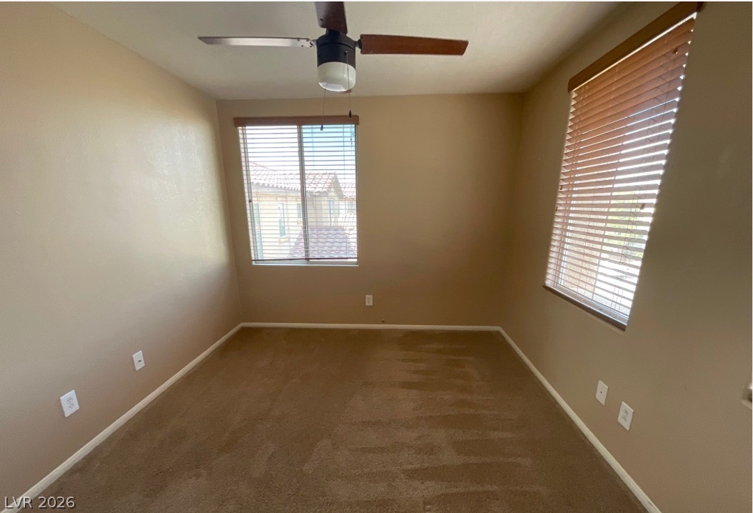10841 Paradise Road Henderson, NV 89052 - Photo 23 of 35 An airy bedroom with a ceiling fan, plush carpeting, and sun-filled windows offering neighborhood views.
