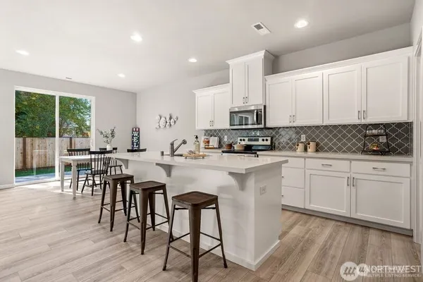 a kitchen with stainless steel appliances granite countertop a stove a sink a refrigerator with white cabinets and wooden floor