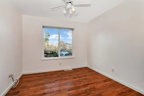 an empty room with wooden floor chandelier fan and windows